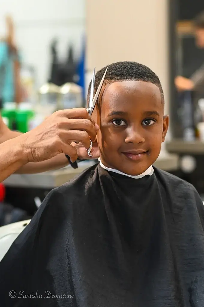 Smiling boy in a black cape while a barber cuts his hair with scissors